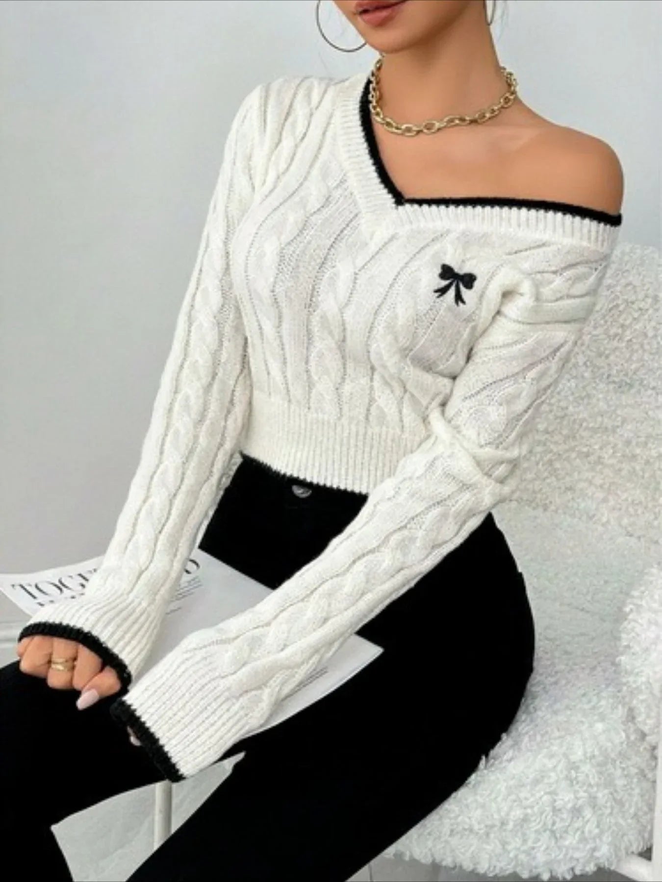 Woman wearing a white cable knit V-neck cropped sweater with black trim, styled off-the-shoulder.