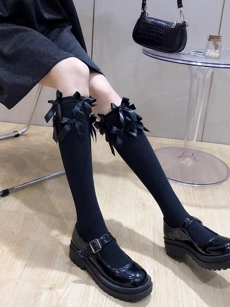 Black knee-high socks with multiple black bows at the cuff, worn with black Mary Jane shoes.