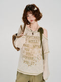 Woman holding a brown tote bag and wearing a cream-colored long-sleeved graphic t-shirt.