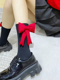 Close-up of black crew socks featuring a prominent red bow on the calf, worn with black patent platform shoes.