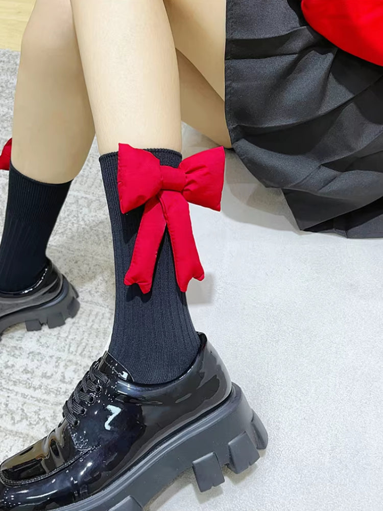 Close-up of black crew socks featuring a prominent red bow on the calf, worn with black patent platform shoes.