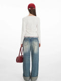 Back view of a woman in a white long-sleeve top with a red floral print and red trim, and distressed denim jeans.