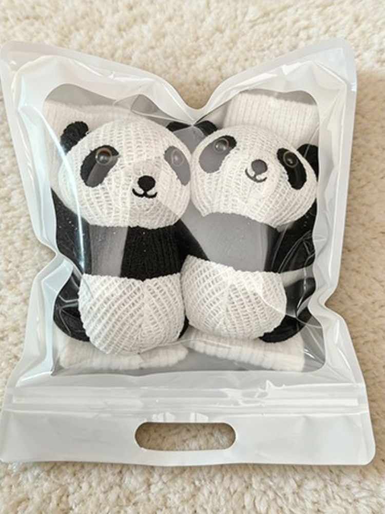 A pair of white crew socks with panda appliques packaged in a clear zip-top bag