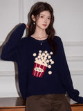 Woman leaning on a surface, wearing a navy blue knit sweater with popcorn design