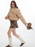 Woman in motion wearing a beige cropped puffer jacket, plaid skirt, and leg warmers.