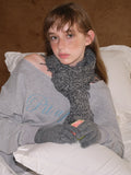 Young woman wearing a grey graphic print sweatshirt with a distressed v-neck, a grey knitted scarf with fringe detail, and grey knitted gloves.