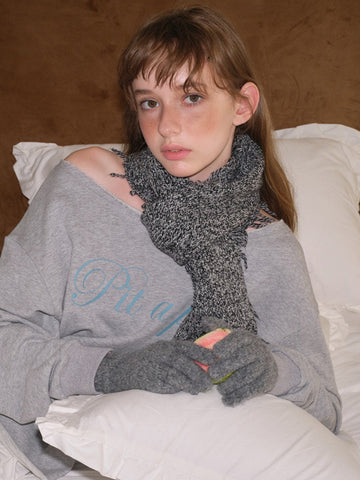 Young woman wearing a grey graphic print sweatshirt with a distressed v-neck, a grey knitted scarf with fringe detail, and grey knitted gloves.