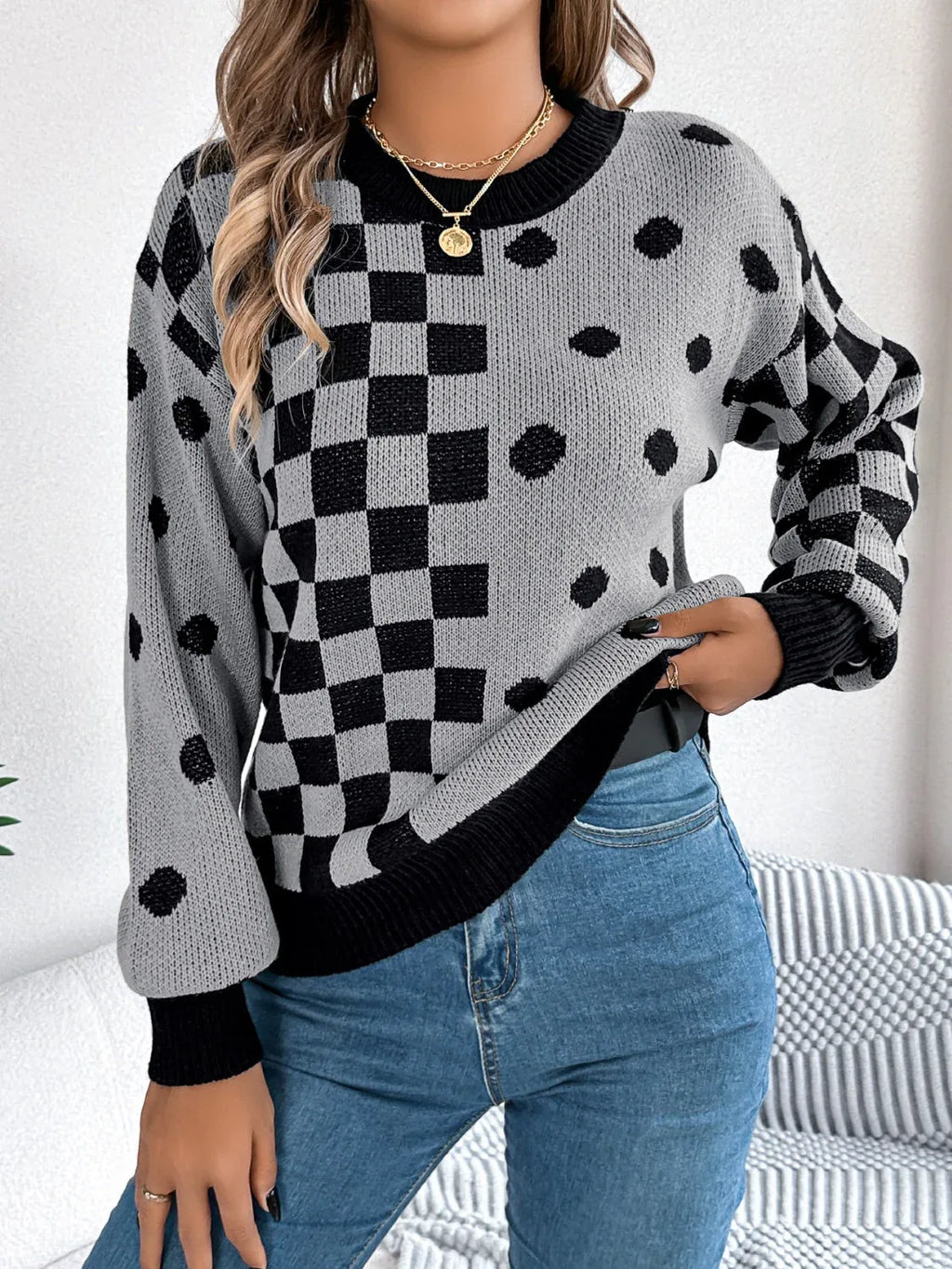Close-up of a woman's torso wearing a grey knit sweater with black checkerboard and polka dot patterns, and blue jeans.