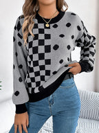 Close-up of a woman's torso wearing a grey knit sweater with black checkerboard and polka dot patterns, and blue jeans.