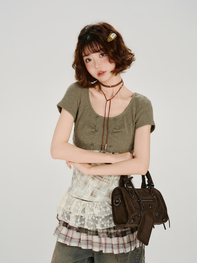 Woman wearing a green ribbed knit short sleeve top with a white and brown patterned corset-style overlay and lace trim.