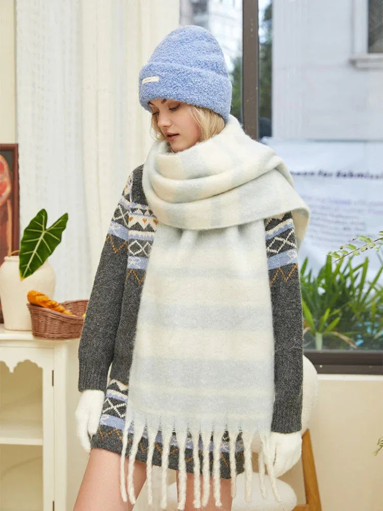 Woman wearing a light blue knit beanie, a large white and blue striped knit scarf with fringe, a grey knit sweater with a diamond pattern, white gloves, and white knee-high socks.