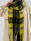 woman wearing a grey coat and light pants with a pink and tan plaid scarf around her neck