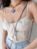 Detail of a white camisole top featuring intricate eyelet embroidery and a ruched bust.