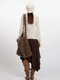 Back view of a woman wearing a cream ribbed knit turtleneck sweater, brown asymmetrical hem skirt, and a brown faux fur shoulder bag.