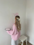 Woman with a bow in her hair holding a plate while wearing a pink cable knit sweater