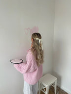 Woman with a bow in her hair holding a plate while wearing a pink cable knit sweater
