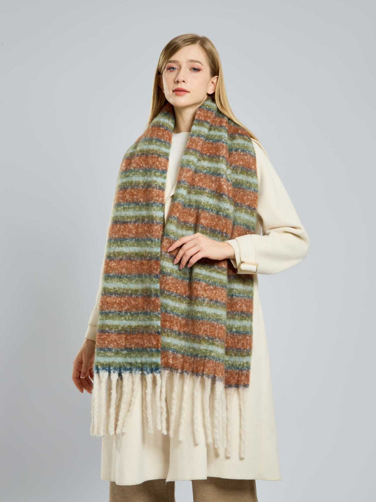 Woman wearing a long, wide scarf with horizontal stripes in rust, light blue, and green, featuring cream fringe at the ends.