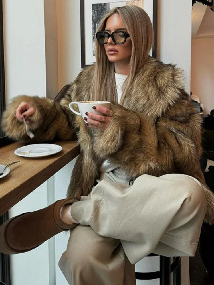 Fashionable woman in a cozy faux fur coat, seated at a cafe table.