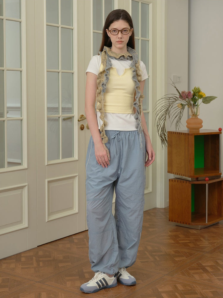 Woman wearing a white t-shirt, yellow tank top, textured scarf, and light blue drawstring trousers with white piping.