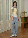 Full length view of a woman styled in casual attire, featuring layered tops and wide-leg pants.