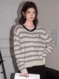 Woman wearing a cream and navy striped button-up knit cardigan with a V-neckline and embroidered detail.