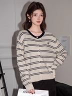 Woman wearing a cream and navy striped button-up knit cardigan with a V-neckline and embroidered detail.