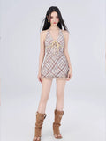 Full body shot of a woman in a plaid halter mini dress with a tie front and ruffled hem, wearing brown boots.