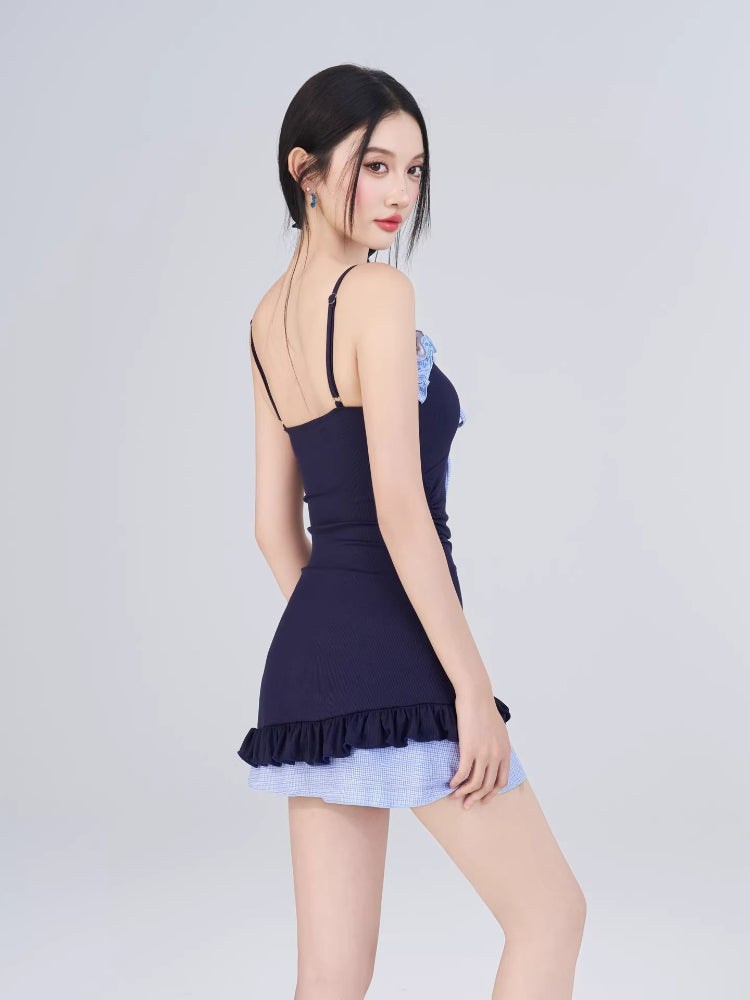 Rear view of woman in navy one-piece swimsuit with blue gingham skirt overlay and white sheer cardigan