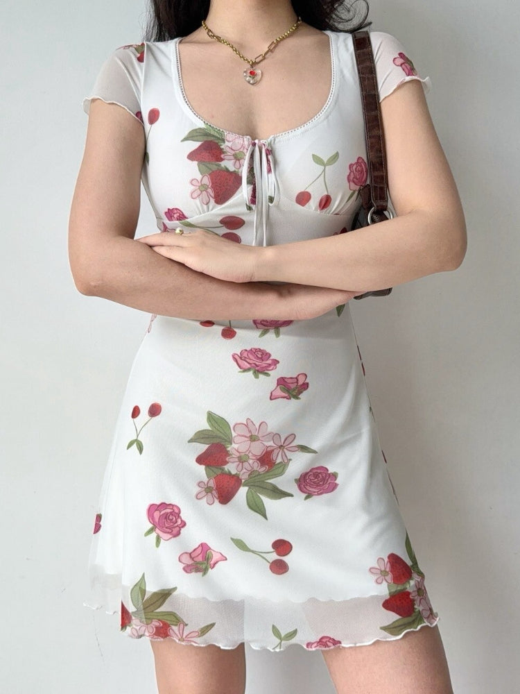 Woman wearing a white short-sleeved mesh dress with a strawberry, cherry, and rose print.