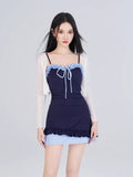 Woman in navy one-piece swimsuit with blue gingham skirt overlay and white sheer cardigan
