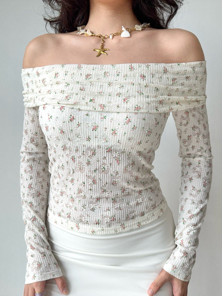 Woman wearing a white off-the-shoulder top with a floral print and long sleeves.