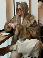 Woman wearing a brown faux fur jacket and beige pants, holding a cup of coffee.