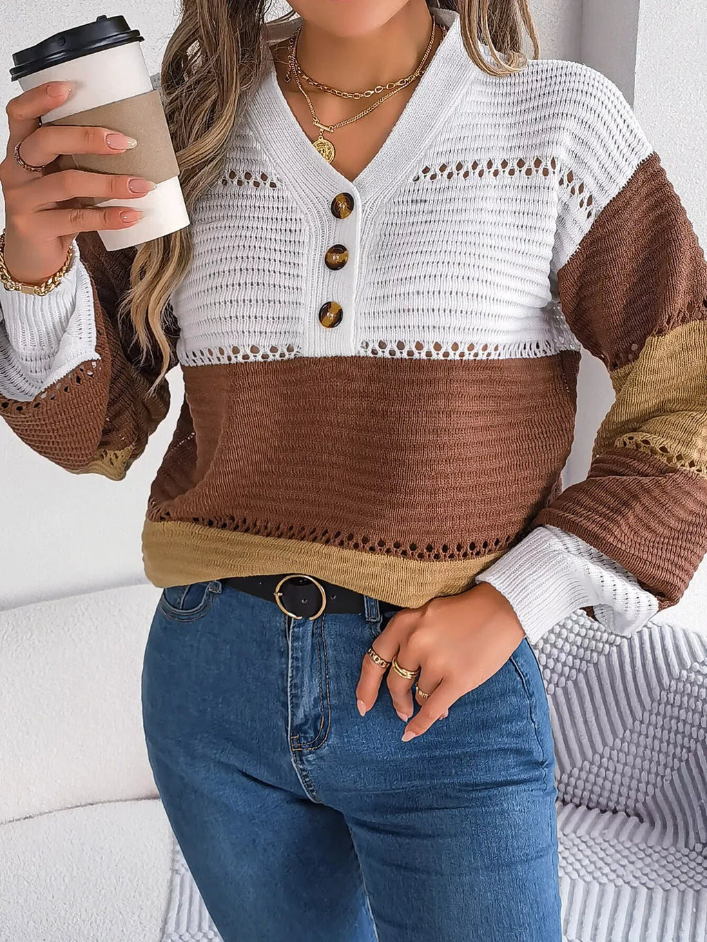 Woman in blue jeans and a color block knit sweater, holding a coffee cup.
