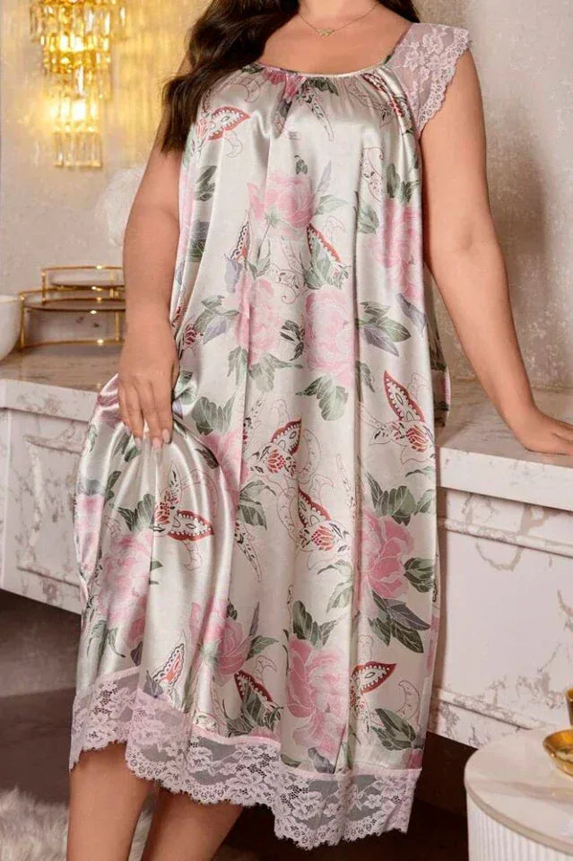 Woman leaning against a counter in a light grey satin midi nightgown with a pink floral and butterfly print and lace trim.