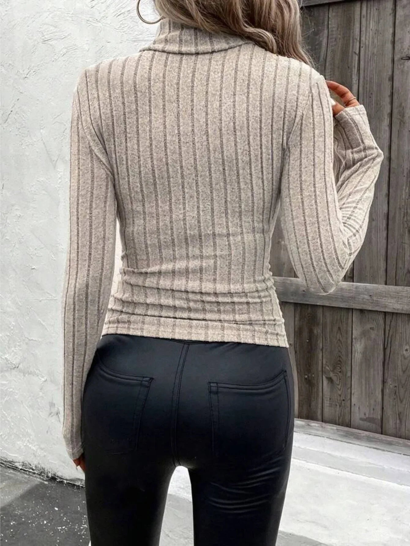 Back view of a woman in a ribbed knit beige turtleneck top.