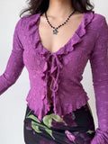 Front view of a woman in a purple textured mesh long-sleeve top with ruffled trim and a tie-front detail.