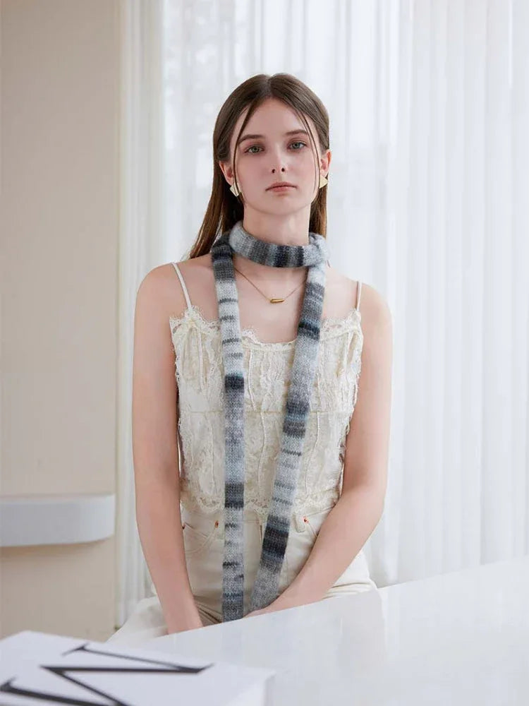 Front view of a woman wearing a casual outfit with a long, multi-toned grey and black striped knit scarf.