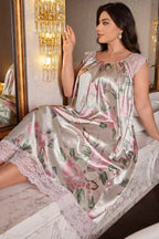 Woman sitting on a marble counter wearing a light grey satin nightgown with a pink floral and butterfly print, lace cap sleeves, and lace hem.