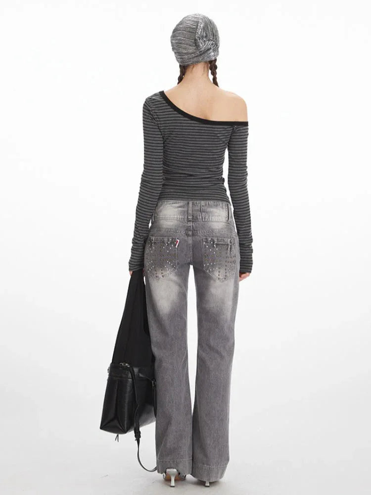 Back view of a woman wearing a grey and black striped off-the-shoulder long sleeve top and grey wash jeans with embellished back pockets.
