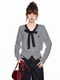 Woman wearing a grey knit cardigan with navy trim and bow