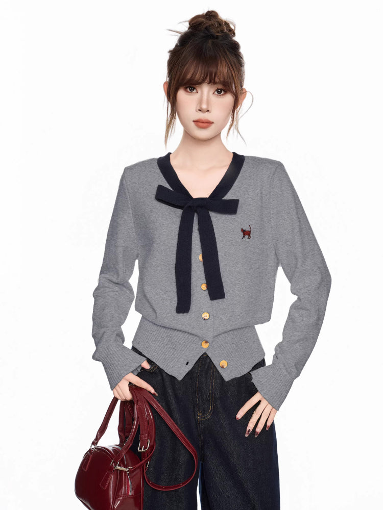 Woman wearing a grey knit cardigan with navy trim and bow