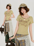 Full-body view of a woman wearing the light green graphic print t-shirt and a layered plaid and textured skirt, accessorized with a cap and a handbag.