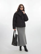 Full body shot of a woman in a black puffer jacket, grey skirt, and black tote bag
