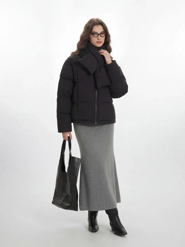 Full body shot of a woman in a black puffer jacket, grey skirt, and black tote bag