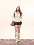 Full body shot of a woman in a cream long-sleeve top, brown shorts, and cream slouchy boots.