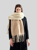 Woman wearing a beige oversized scarf with fringe detail