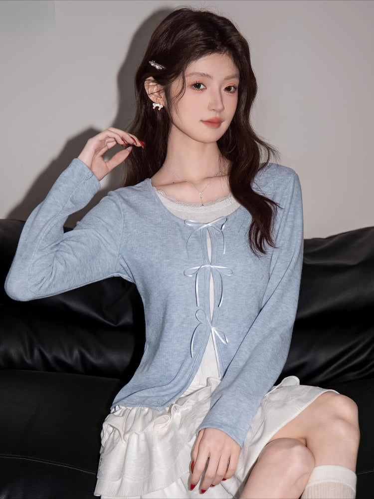Close-up of a woman's upper body wearing a light blue knit cardigan with white bow tie closures.
