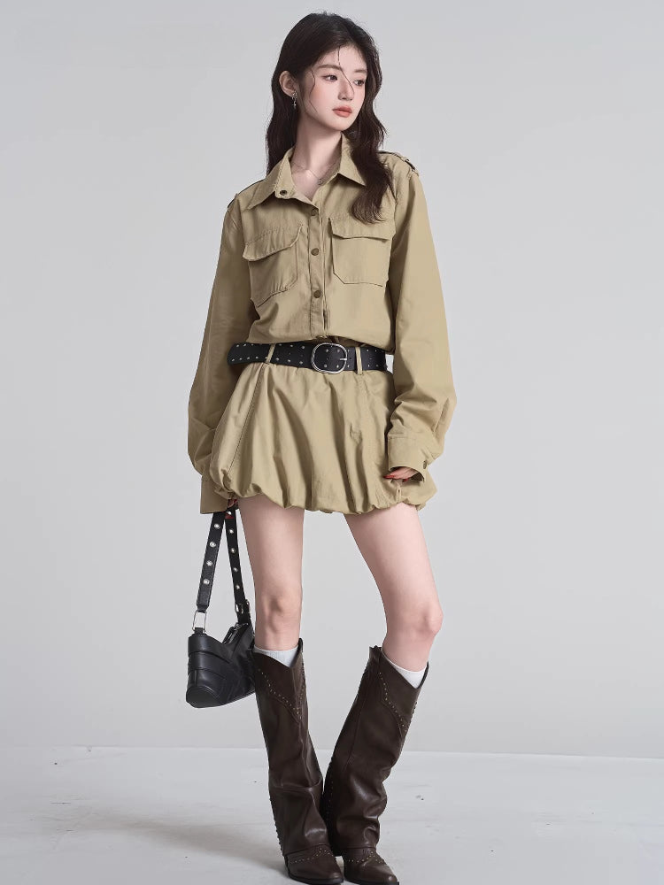 Full body shot of a woman in a khaki camp collar shirt dress with a gathered skirt, accessorized with a black studded belt and dark brown boots.