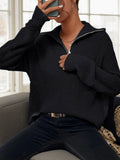 Woman sitting on a couch wearing a black knit half-zip sweater.