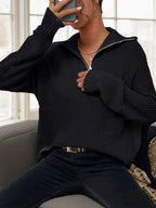 Woman sitting on a couch wearing a black knit half-zip sweater.